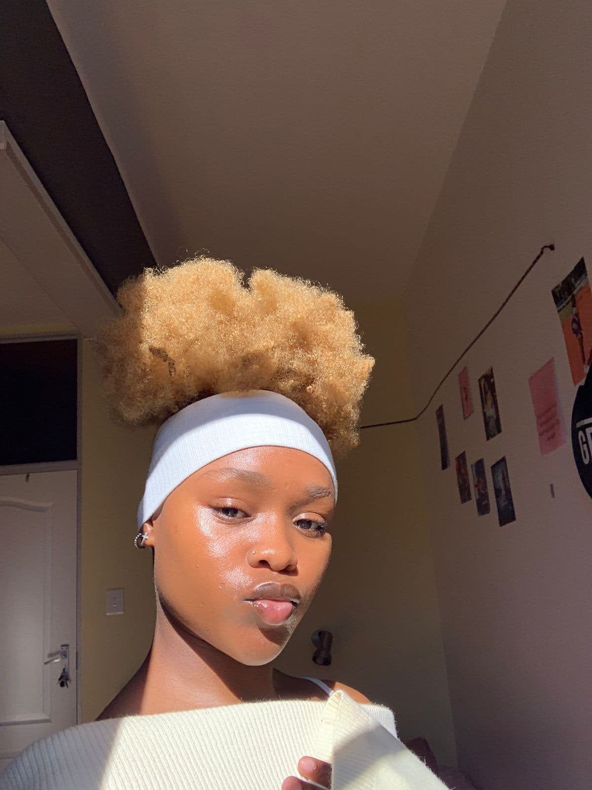 Sunlit young Black woman with a blonde afro puff, white headband, and glowing skin.
