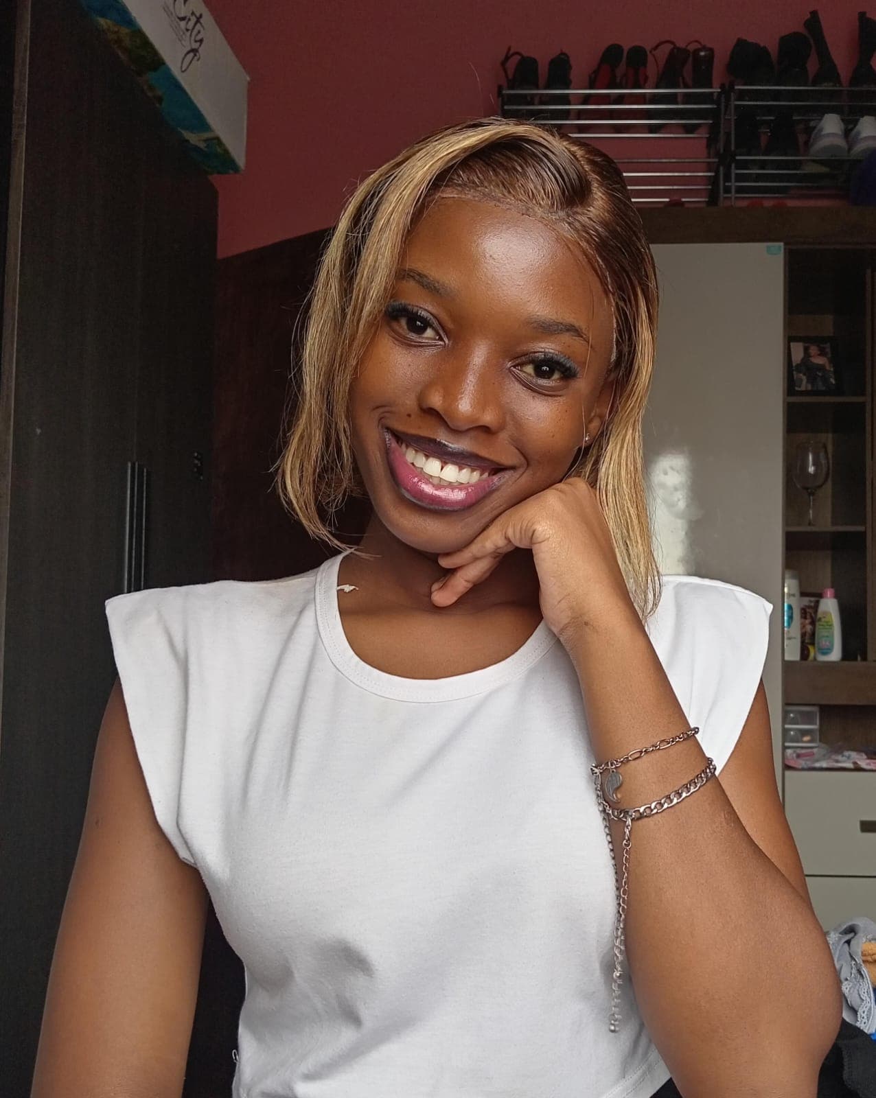 Smiling Black woman with blonde bob hair, wearing a white top, hand under her chin.