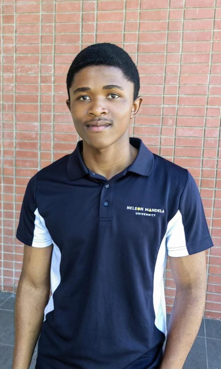 Young man wearing a navy Nelson Mandela University polo shirt against a red brick wall.