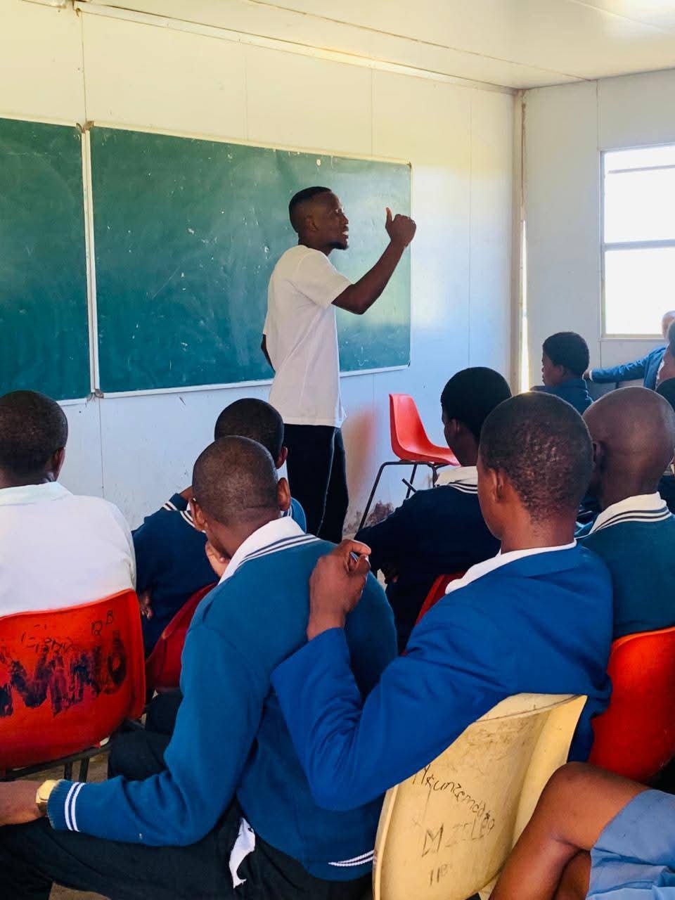 A teacher gives a thumbs-up to students wearing blue uniforms in a classroom.
