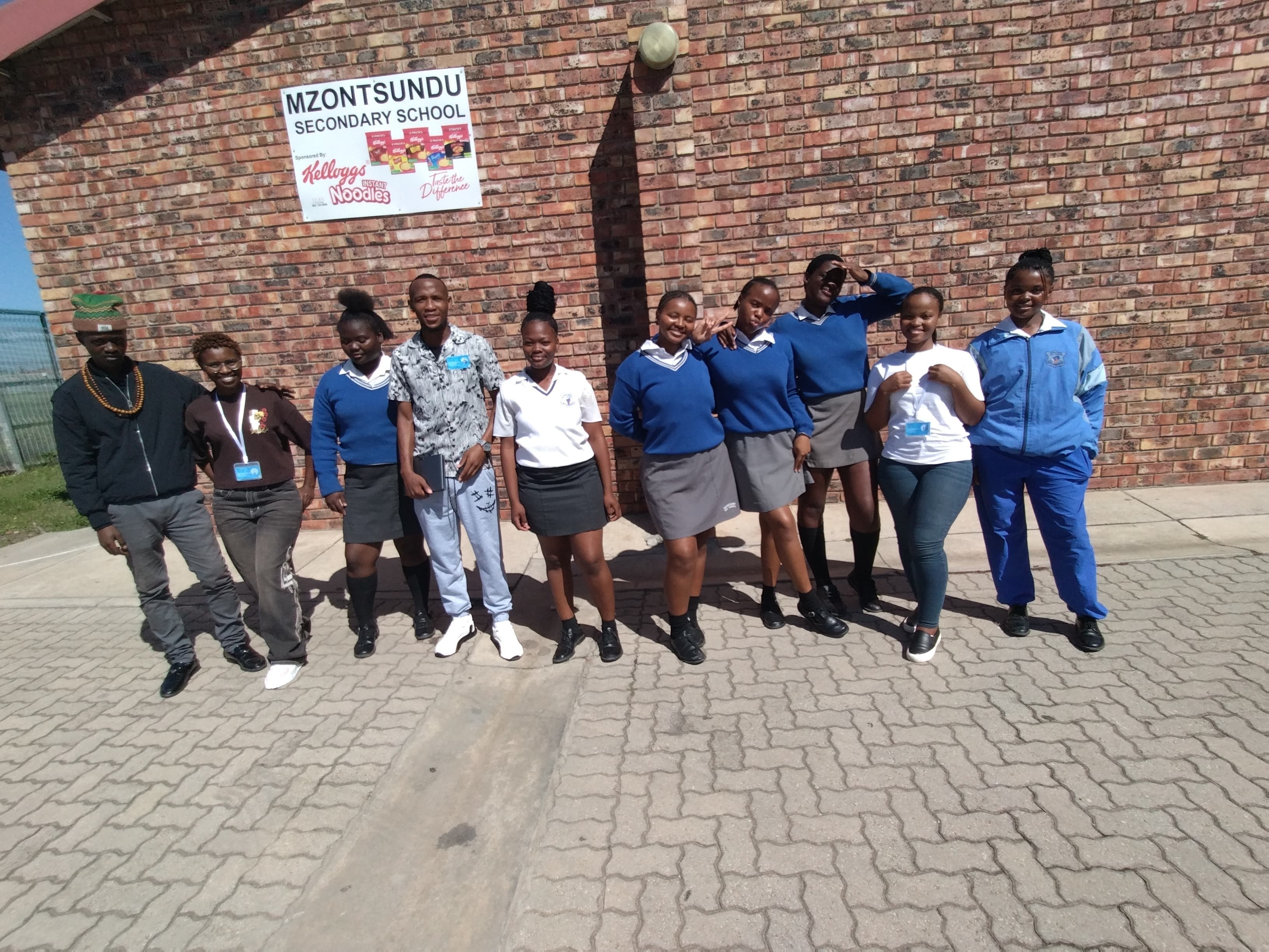 Students and staff pose outside Mzontsundu Secondary School in front of a brick wall.
