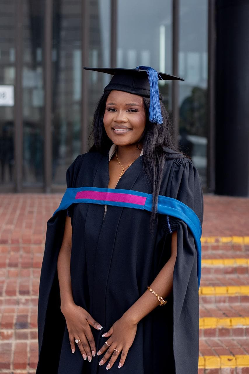 Smiling young Black woman in a black graduation gown and cap with a blue tassel.